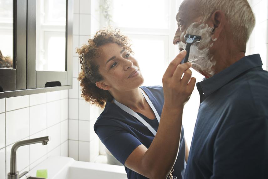 Home health aide helping older man shave