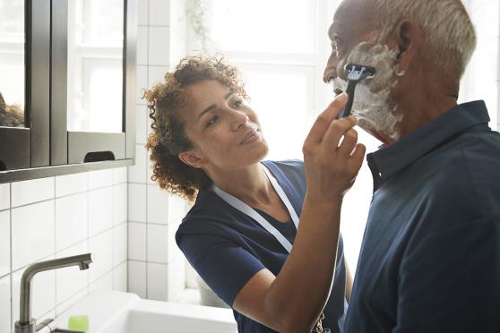 Home health aide helping older man shave